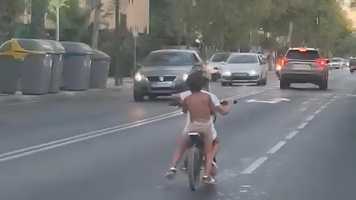 dos niños circulan en moto y sin casco por el carril central de una concurrida avenida